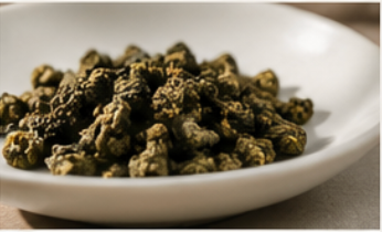 Rolled green tea buds piled in a shallow white ceramic bowl, photographed close-up with a soft blurred background.