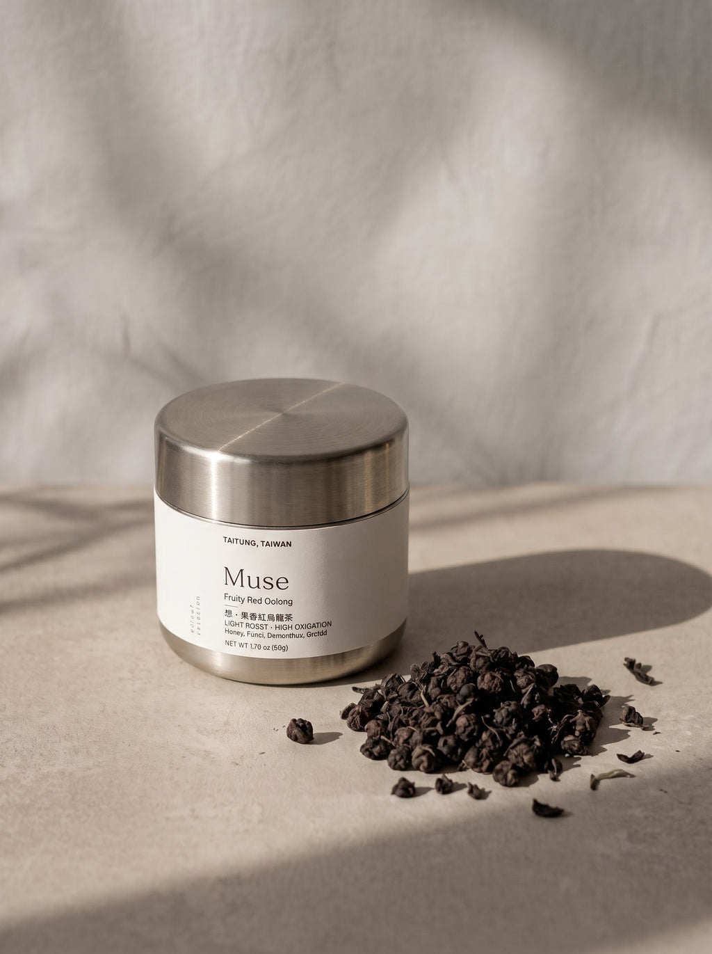A jar of Nature's Lane Muse Face Red Cleansing Milk with a brushed silver lid and white label, placed on a textured beige surface next to a small pile of dark dried tea leaves under soft, dramatic shadows.